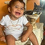 toddler, child, smiling, cat, pet, indoor, furniture, cat_tree, white_clothing, necklace, orange_wall, happy, playful, young_child, cute, domestic_animal, sitting, face, earrings, home