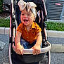 Kataleia is registered to the contest to win money with this photo: toddler, child, stroller, smiling, headband, orange_shirt, outdoor, sunlight, happy, holding, seat, jeans, concrete, grass, parking_lot, air_conditioner, metal_bar, baby, cute, person