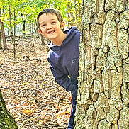 Kayden is registered to the contest to win money with this photo: child, boy, tree, forest, autumn, leaves, nature, outdoor, playful, smiling, hoodie, casual_clothing, daylight, trunk, woods, young, person, fun, seasonal, environment