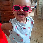 Lilly a rejoint le concours — aidez-le/la à gagner de superbes lots ! child, clothing, curly_hair, cute, face, furniture, happy, home_interior, indoor, person, pink_sunglasses, playful, portrait, red_chair, shorts, smiling, tiled_floor, toddler, watermelon_shirt, wooden_dresser