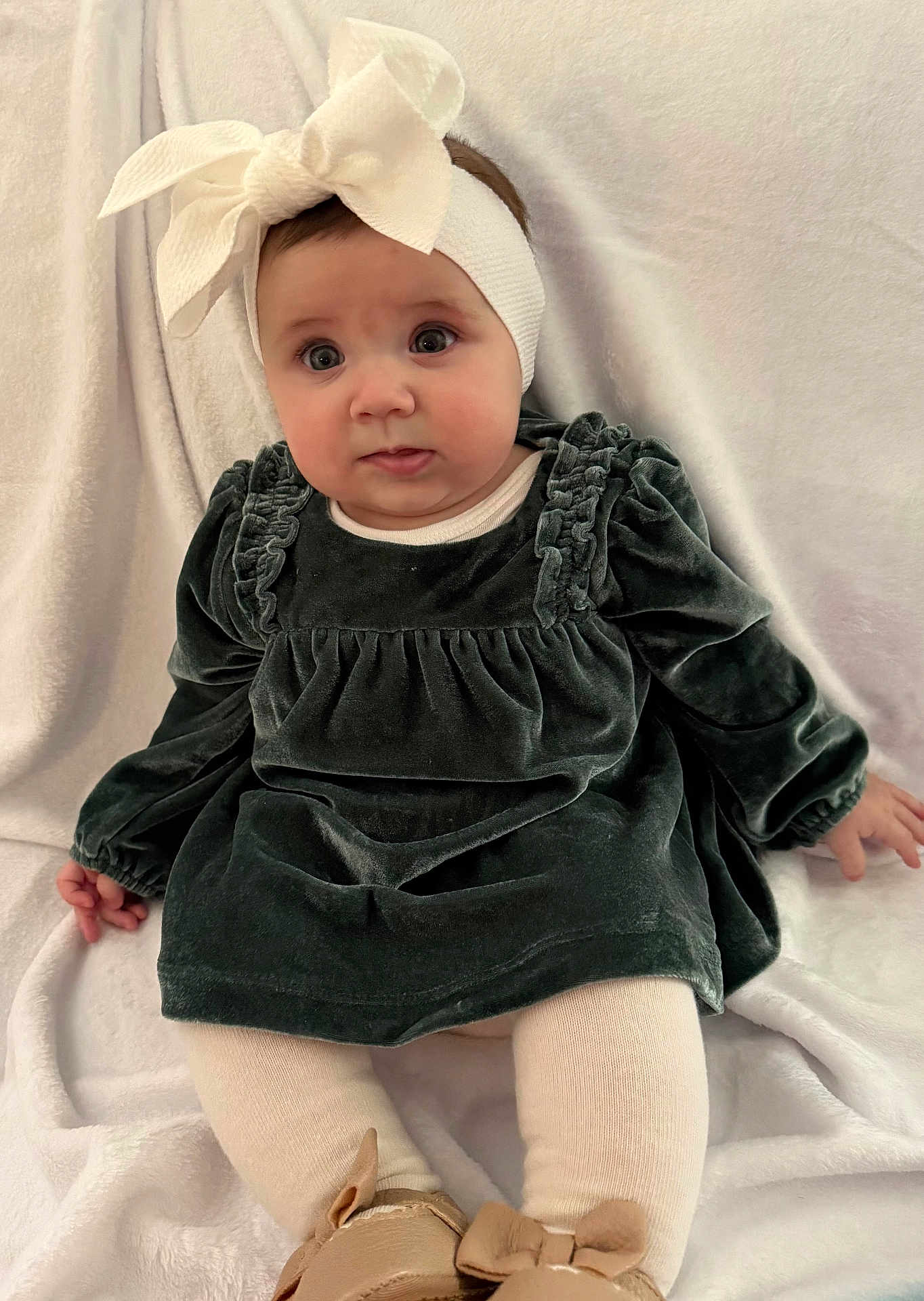Angelina is registered to the contest to win money with this photo: baby, child, white_bow, headband, green_dress, velvet, sitting, blanket, white_tights, soft_background, curious_expression, indoor, footwear, brown_shoes, cute, portrait, infant, chubby_cheeks, long_sleeves, hands