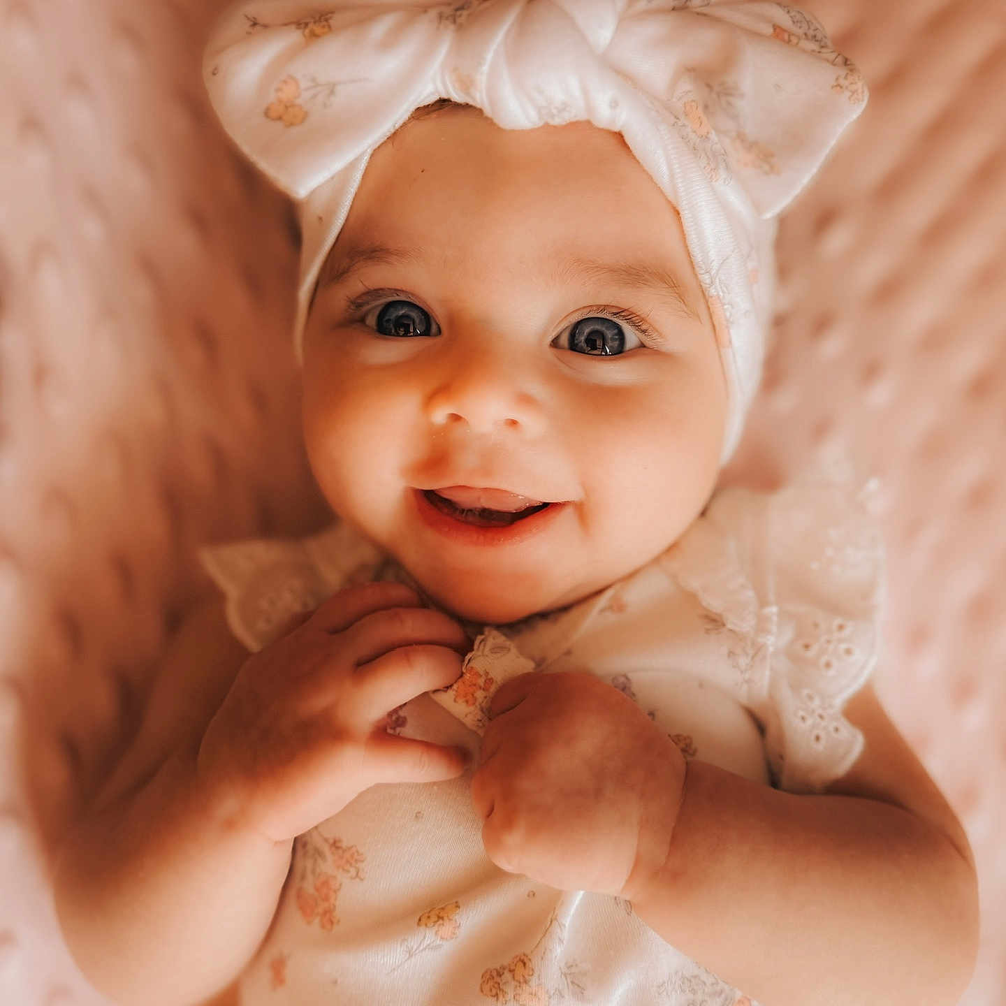 Amaya is registered to the contest to win money with this photo: baby, blanket, bow, child, closeup, clothing, cute, eyes, face, hands, happy, headband, infant, lying_down, pink, portrait, skin, smiling, soft, texture