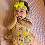 baby, child, infant, smiling, cute, yellow_bow, curly_hair, pink_blanket, lemon_pattern, onesie, happy, playful, hand_in_mouth, portrait, lying_down, soft_texture, indoors, adorable, young_child, headband