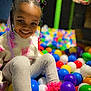 child, smiling, ball_pit, colorful, braided_hair, pink_beads, playground, happy, indoor, toy, legs, sitting, casual_clothing, young, cute, fun, leisure, person, play, entertainment