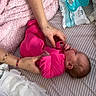 baby, infant, child, pink_clothing, adult, hands, face, sleeping, lying_down, bed, blanket, pacifier, baby_wipes, diaper, changing, nursery, indoor, textile, caregiving, portrait