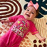 Evangeline is registered to the contest to win money with this photo: baby, child, pink_bow, pink_outfit, barbie, smiling, lying_down, patterned_mat, happy, cute, infant, face, head, clothing, person, indoor, cheerful, young_child, baby_girl, playtime