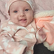 Olivia is registered to the contest to win money with this photo: baby, infant, smile, pink_clothing, hat, blanket, bunny_pattern, happy, cute, cozy, face, tongue_out, sitting, indoor, child, soft_texture, couch, apparel, person, portrait