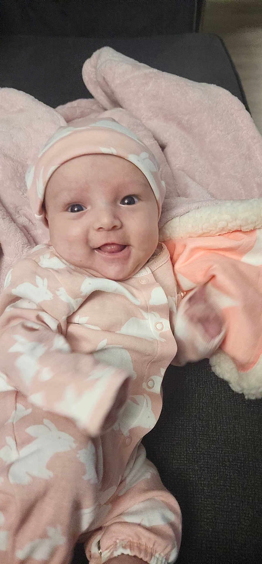 Olivia is registered to the contest to win money with this photo: baby, infant, smile, pink_clothing, hat, blanket, bunny_pattern, happy, cute, cozy, face, tongue_out, sitting, indoor, child, soft_texture, couch, apparel, person, portrait