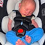 newborn, baby, sleeping, car_seat, safety_harness, blue_pants, grey_shirt, infant, tiny_toes, head_support, black_fabric, close_up, indoors, child, peaceful, resting, seat_belt, baby_clothing, soft_padding, infant_care
