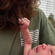 Dakota is registered to the contest to win money with this photo: baby, newborn, hand, fingers, beard, facial_hair, lips, person, green_shirt, indoor, window_blinds, closeup, skin, expression, interaction, touch, care, family, tenderness, portrait