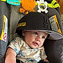 baby, child, hat, cap, black, tshirt, toy, seat, infant, blue_eyes, face, cute, indoor, clothing, pattern, expression, person, comfort, play, closeup