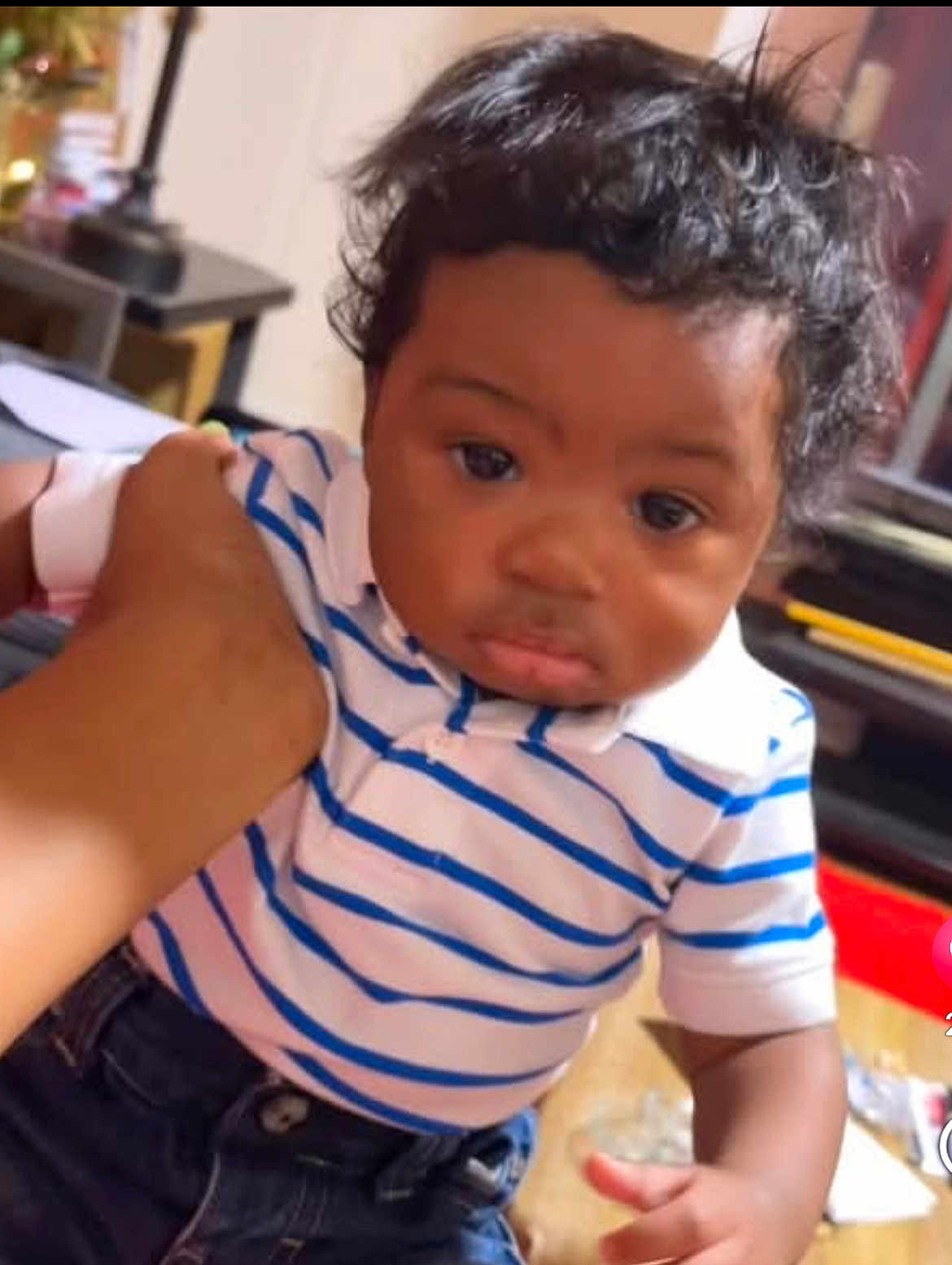 Tylee is registered to the contest to win money with this photo: baby, child, striped_shirt, polo_shirt, jeans, indoor, hand, person, curly_hair, furniture, lamp, table, casual_clothing, portrait, young_child, cute, holding, skin, face, expression