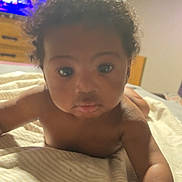 Tylee is registered to the contest to win money with this photo: baby, child, infant, curly_hair, blanket, bed, indoor, face, eyes, skin, arm, expression, pout, person, young, portrait, room, television, furniture, lighting