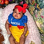 Azalea joined the competition — help win amazing prizes! baby, infant, child, cushion, pink, red_bow, blue_shirt, yellow_skirt, apples, basket, floral_background, wooden_floor, soft_texture, crown_patch, cute, portrait, indoors, smiling, headband, person