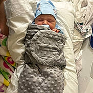 John joined the competition — help win amazing prizes! newborn, baby, blanket, blue_hat, bed, fabric, striped_cloth, colorful_cloth, sleeping, infant, wrapped, soft_texture, cute, resting, indoors, person, child, cozy, nursery, peaceful