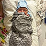 newborn, baby, blanket, blue_hat, bed, fabric, striped_cloth, colorful_cloth, sleeping, infant, wrapped, soft_texture, cute, resting, indoors, person, child, cozy, nursery, peaceful