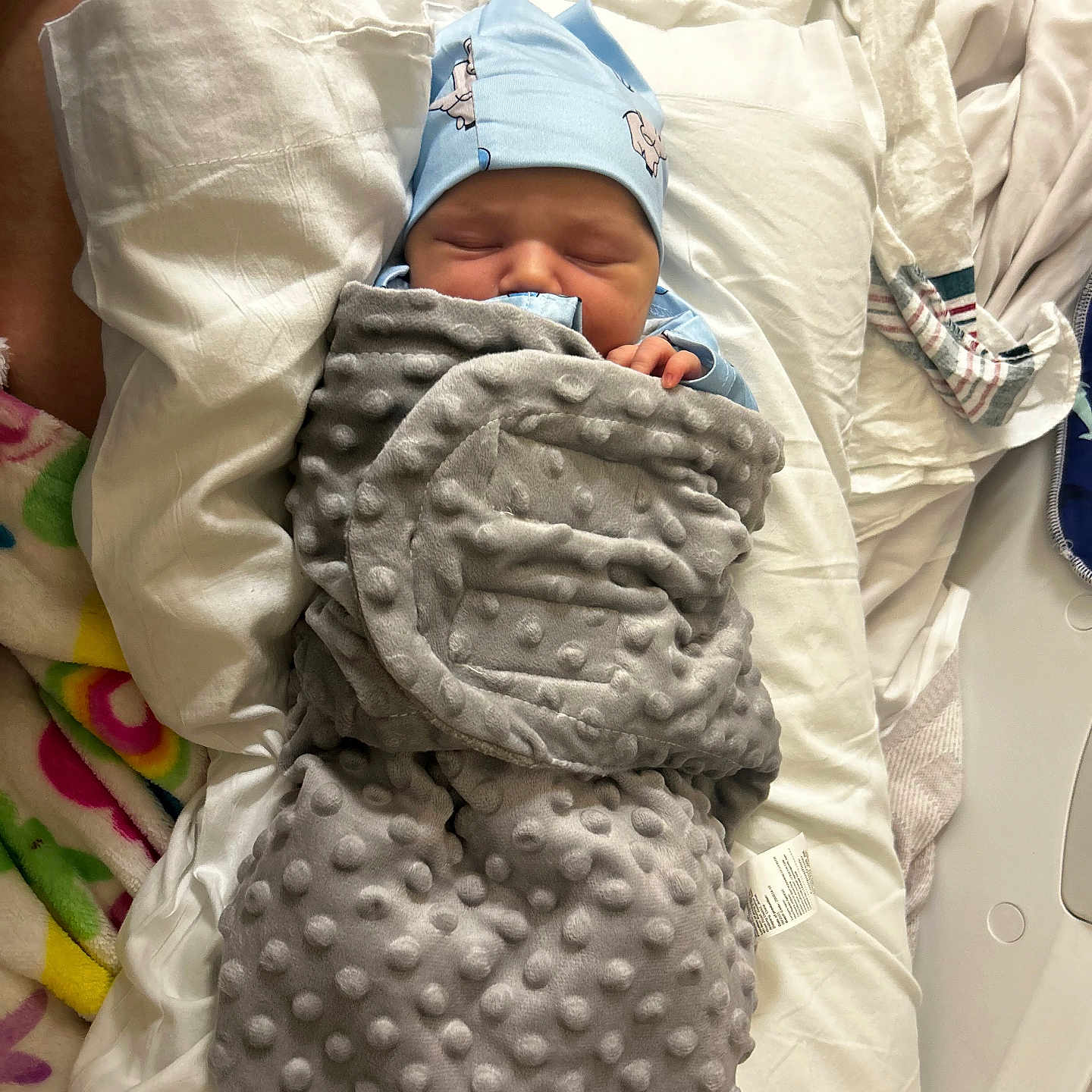 John joined the competition — help win amazing prizes! newborn, baby, blanket, blue_hat, bed, fabric, striped_cloth, colorful_cloth, sleeping, infant, wrapped, soft_texture, cute, resting, indoors, person, child, cozy, nursery, peaceful