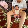 baby, woman, hammock, smile, indoor, floor, tile_floor, sitting, happy, person, clothing, red_nails, blanket, pattern, foot, hand, face, hair, ring, cozy