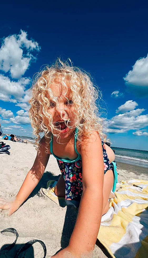 Evie is registered to the contest to win money with this photo: beach, blue, brassiere, cloud, eyewear, fun, happy, horizon, leisure, people_in_nature, people_on_beach, person, recreation, sand, sky, surfer_hair, swimwear, thigh, toddler, travel