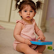 Lia joined the competition — help win amazing prizes! baby, book, carpet, child, curious, cute, floor, hair_bows, indoor, infant, looking, one_person, person, pigtails, pink_outfit, portrait, sitting, toddler, toy, young_child