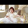 Lia joined the competition — help win amazing prizes! birthday_cake, cake, candle, celebration, child, curious, cute, decorations, furniture, glass_table, happy, indoor, living_room, party, pastel_colors, person, seated, toddler, white_dress, young_child