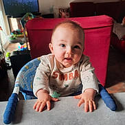 Theo participe au concours pour gagner de l'argent avec cette photo : baby, child, infant, smiling, hands, table, highchair, indoor, living_room, red_couch, toy, face, person, cute, young, clothing, expression, curious, home, furniture