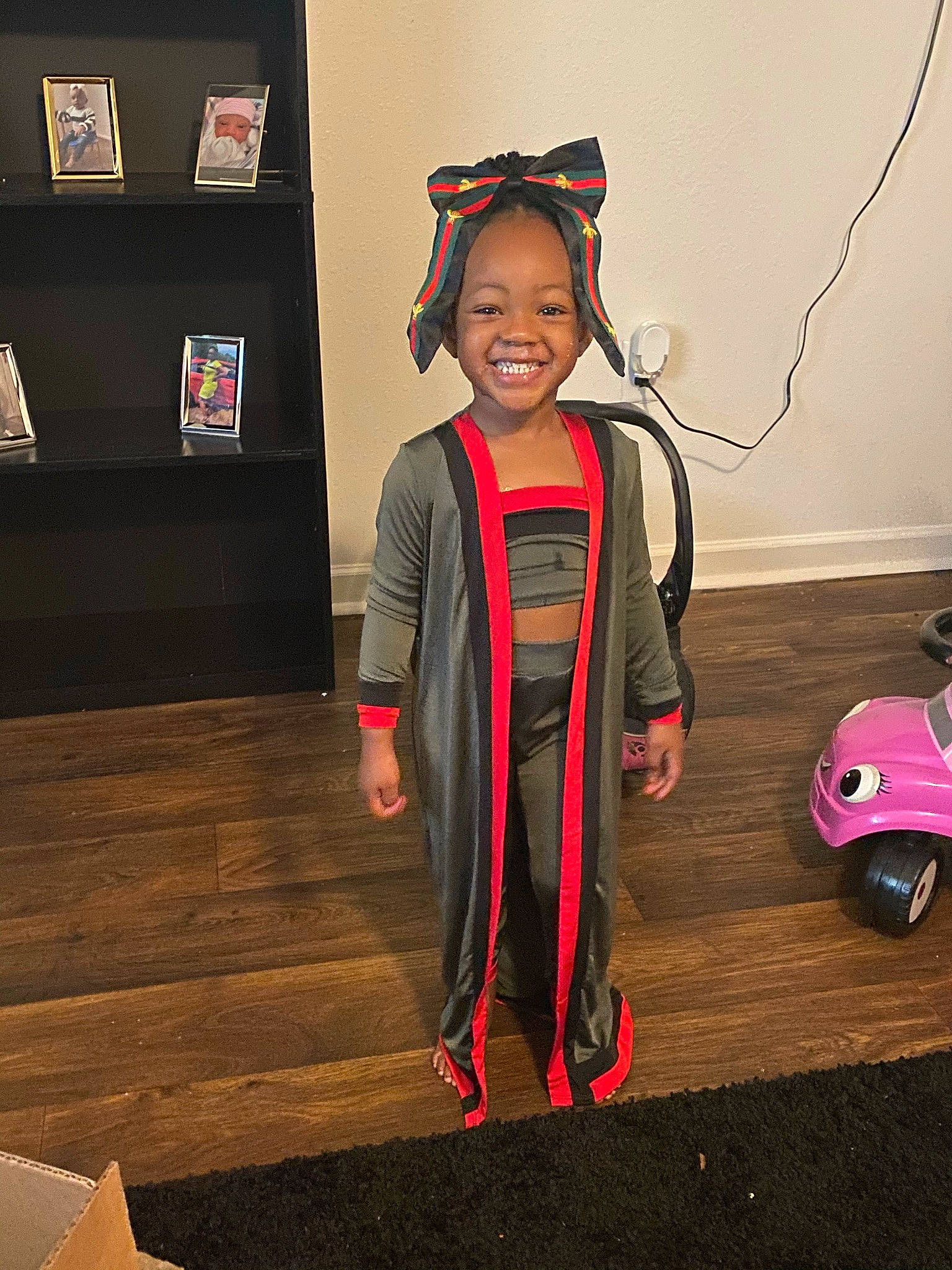 Justice is registered to the contest to win money with this photo: child, costume, event, fashion_design, flooring, fun, happy, hardwood, headwear, joy, person, riding_toy, room, smile, standing, toddler, toy, wheel, wood