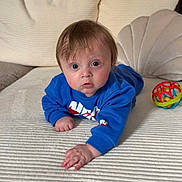 Leandre a rejoint le concours — aidez-le/la à gagner de superbes lots ! baby, blue_sweatshirt, curious, indoors, couch, toy_ball, child, face, hand, expression, fabric, texture, home, young_child, person, sitting, playful, comfortable, soft_lighting, closeup