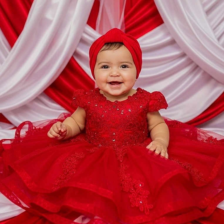 Leslie is registered to the contest to win money with this photo: adorable, baby, background, celebration, child, colorful, cute, dress, fabric, festive, happy, headband, indoor, lace, person, portrait, red_dress, seated, smiling, tulle