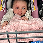 Mianna joined the competition — help win amazing prizes! baby, child, car_seat, blanket, curly_hair, blue_eyes, warning_label, shopping_cart, pink, clothing, infant, person, seat_belt, soft_texture, indoor, cute, portrait, hands, face, expression
