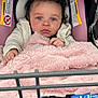 baby, child, car_seat, blanket, curly_hair, blue_eyes, warning_label, shopping_cart, pink, clothing, infant, person, seat_belt, soft_texture, indoor, cute, portrait, hands, face, expression
