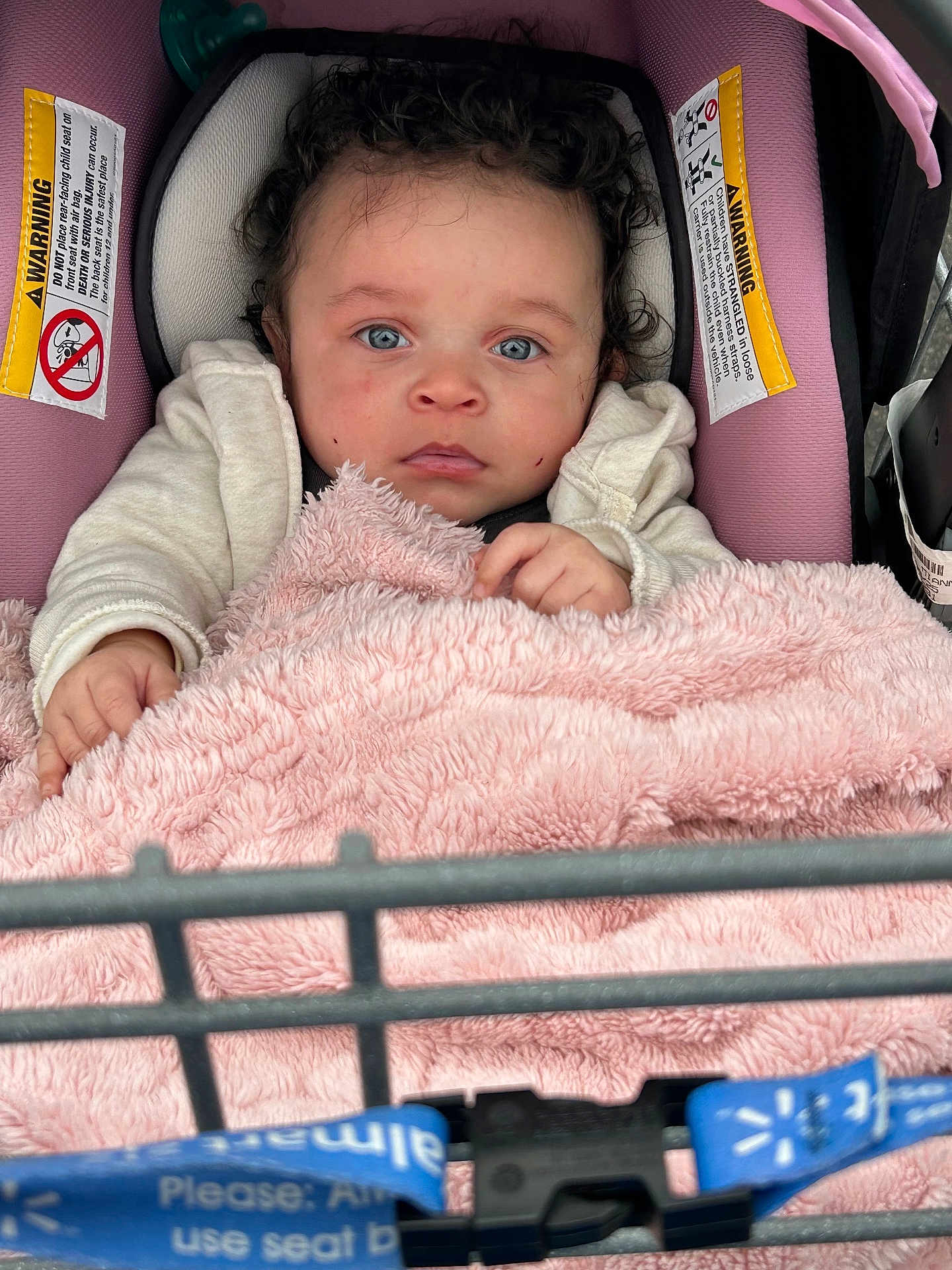 Mianna joined the competition — help win amazing prizes! baby, child, car_seat, blanket, curly_hair, blue_eyes, warning_label, shopping_cart, pink, clothing, infant, person, seat_belt, soft_texture, indoor, cute, portrait, hands, face, expression
