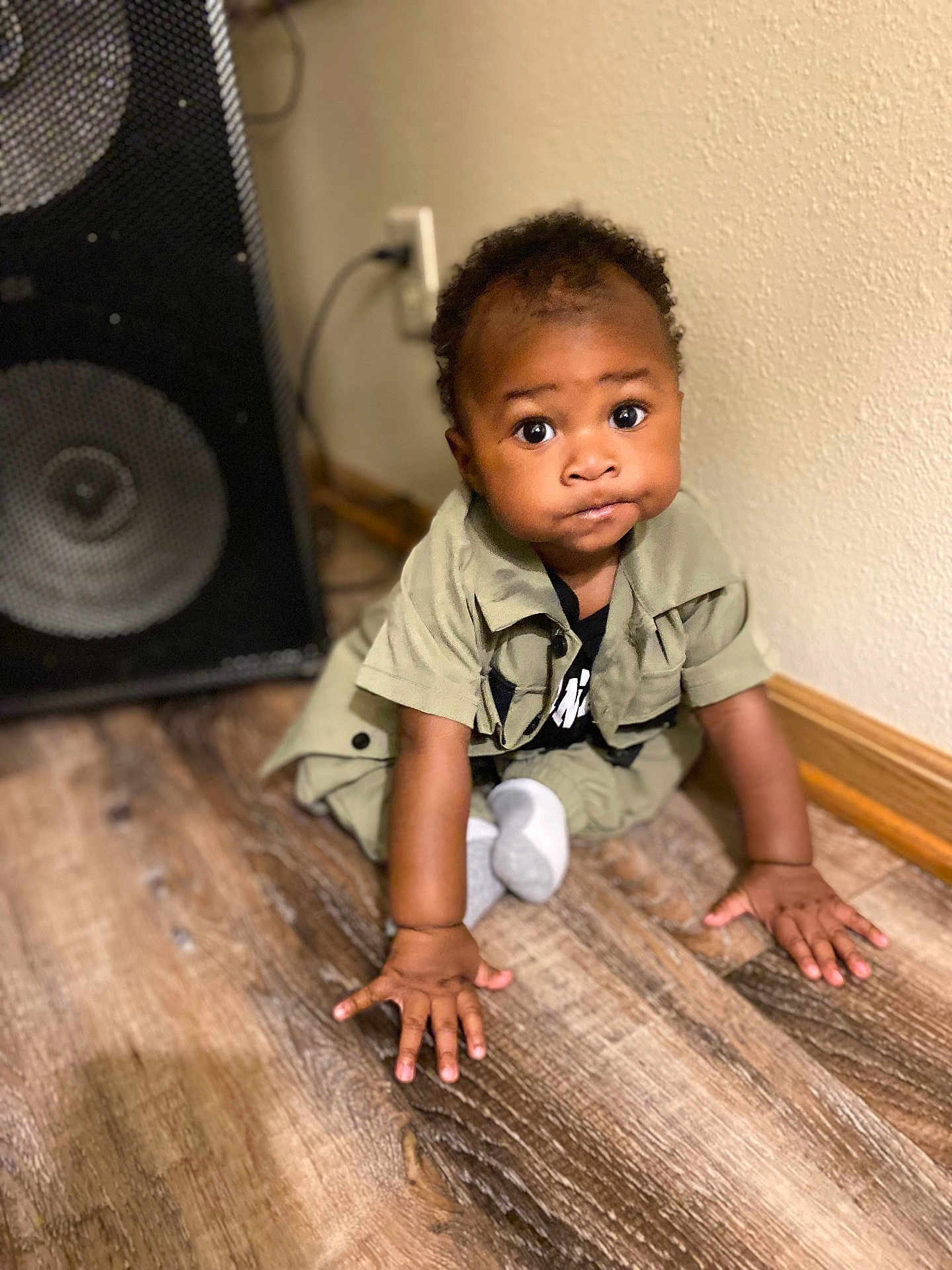 Azarion is registered to the contest to win money with this photo: baby, child, floor, wooden_floor, speaker, wall, curious, sitting, hands, clothing, brown_skin, indoor, expression, young, portrait, cute, crawling, sock, black_hair, room
