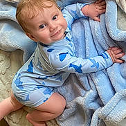 William joined the competition — help win amazing prizes! baby, child, crawling, blue_onesie, shark_pattern, blanket, soft_texture, smiling, happy, indoor, cute, infant, face, hands, feet, light_skin, blond_hair, cozy, playful, portrait