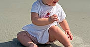 Nora joined the competition — help win amazing prizes! baby, child, beach, sand, ocean, smiling, happy, sunlight, outdoor, toddler, cute, playful, summer, casual_clothing, barefoot, portrait, sitting, nature, vacation, joy