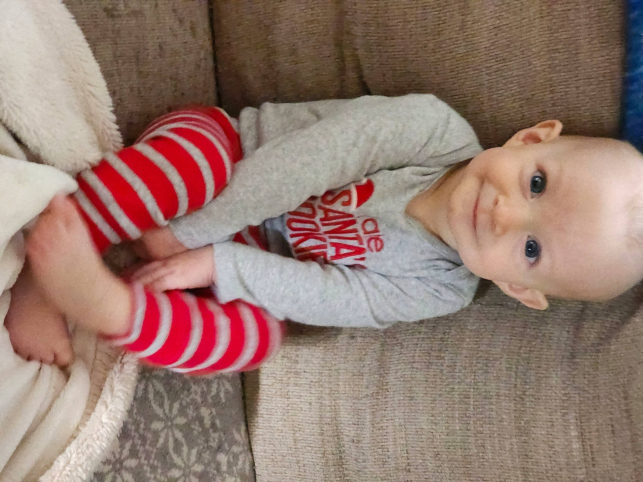 Jaxon is registered to the contest to win money with this photo: baby, baby_toddler_clothing, cheek, child, comfort, couch, elbow, eye, finger, gesture, human_leg, joy, linens, lip, mammal, nose, person, skin, sleeve, smile