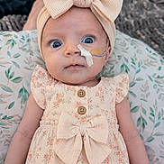 Mia is registered to the contest to win money with this photo: baby, blue_eyes, bow, child, close_up, clothing, cushion, cute, dress, feeding_tube, floral_pattern, headband, indoors, infant, leaf_pattern, medical_tape, newborn, person, portrait, soft_lighting