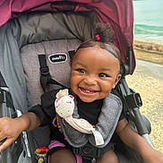 Elyana joined the competition — help win amazing prizes! toddler, child, smiling, stroller, toy, outdoor, water, happy, person, seatbelt, clothing, hair, black_hair, earrings, fabric, baby, playful, cute, seat, daylight