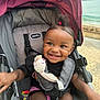 toddler, child, smiling, stroller, toy, outdoor, water, happy, person, seatbelt, clothing, hair, black_hair, earrings, fabric, baby, playful, cute, seat, daylight