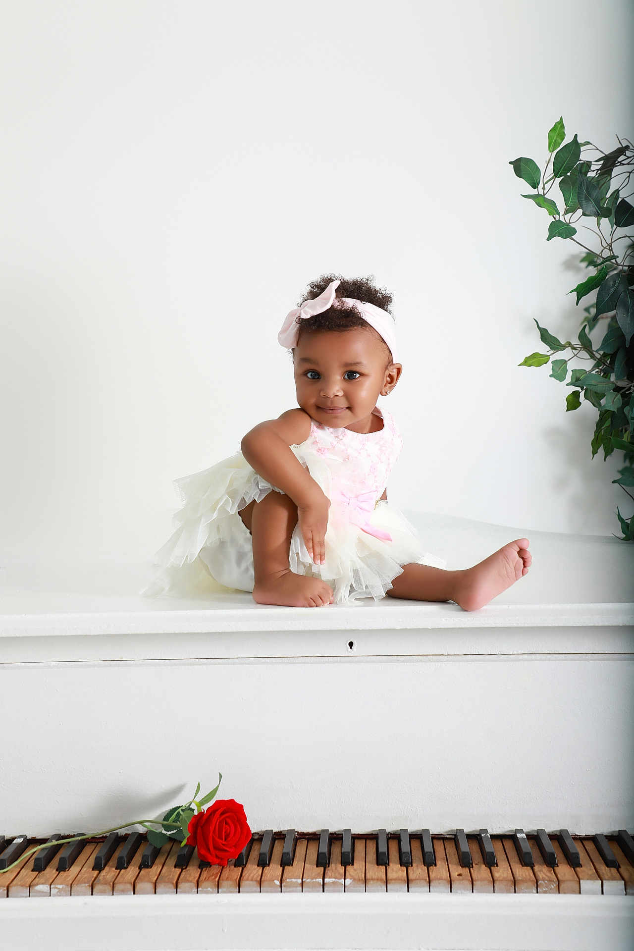 Elyana joined the competition — help win amazing prizes! baby, child, piano, rose, flower, dress, headband, white, pink, smile, cute, sitting, plant, indoor, curly_hair, portrait, furniture, keys, music, decor