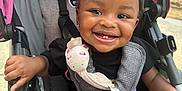 Elyana is registered to the contest to win money with this photo: toddler, child, smiling, stroller, toy, unicorn, outdoor, happy, baby, seatbelt, black_clothing, curly_hair, playful, cute, person, infant, park, sunlight, accessory, joyful