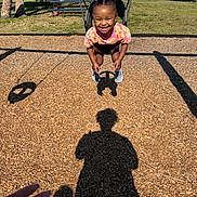 Elyana joined the competition — help win amazing prizes! casual_clothing, child, daylight, fun, grass, hair_beads, hand, happy, outdoor, park_bench, person, pink, playground, recreation, shadow, smile, swing, toddler, trees, woodchips