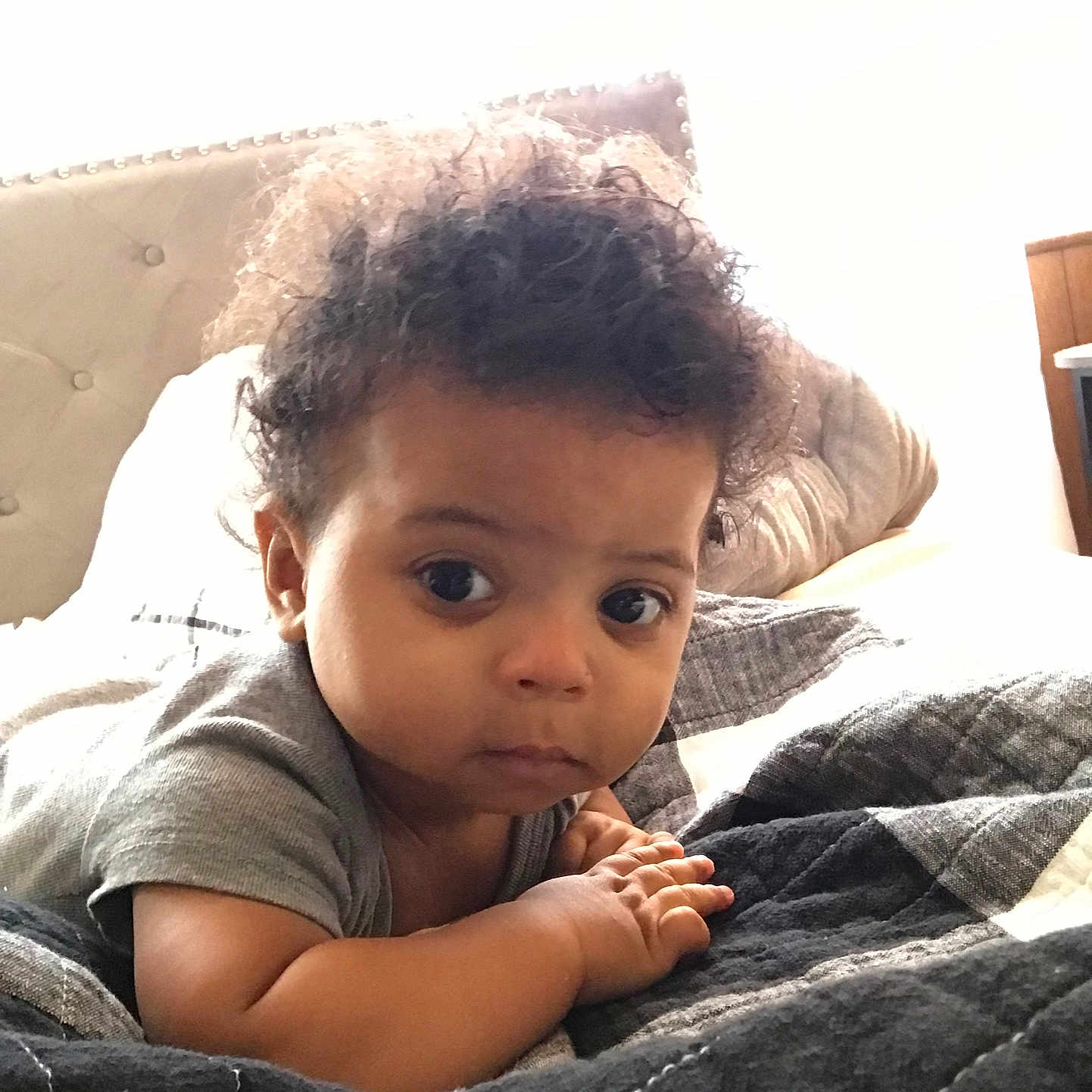 Jabari joined the competition — help win amazing prizes! baby, infant, child, curly_hair, bed, blanket, pillow, indoor, portrait, cute, looking, face, hands, cozy, young, person, clothing, sleeping_area, soft, expression