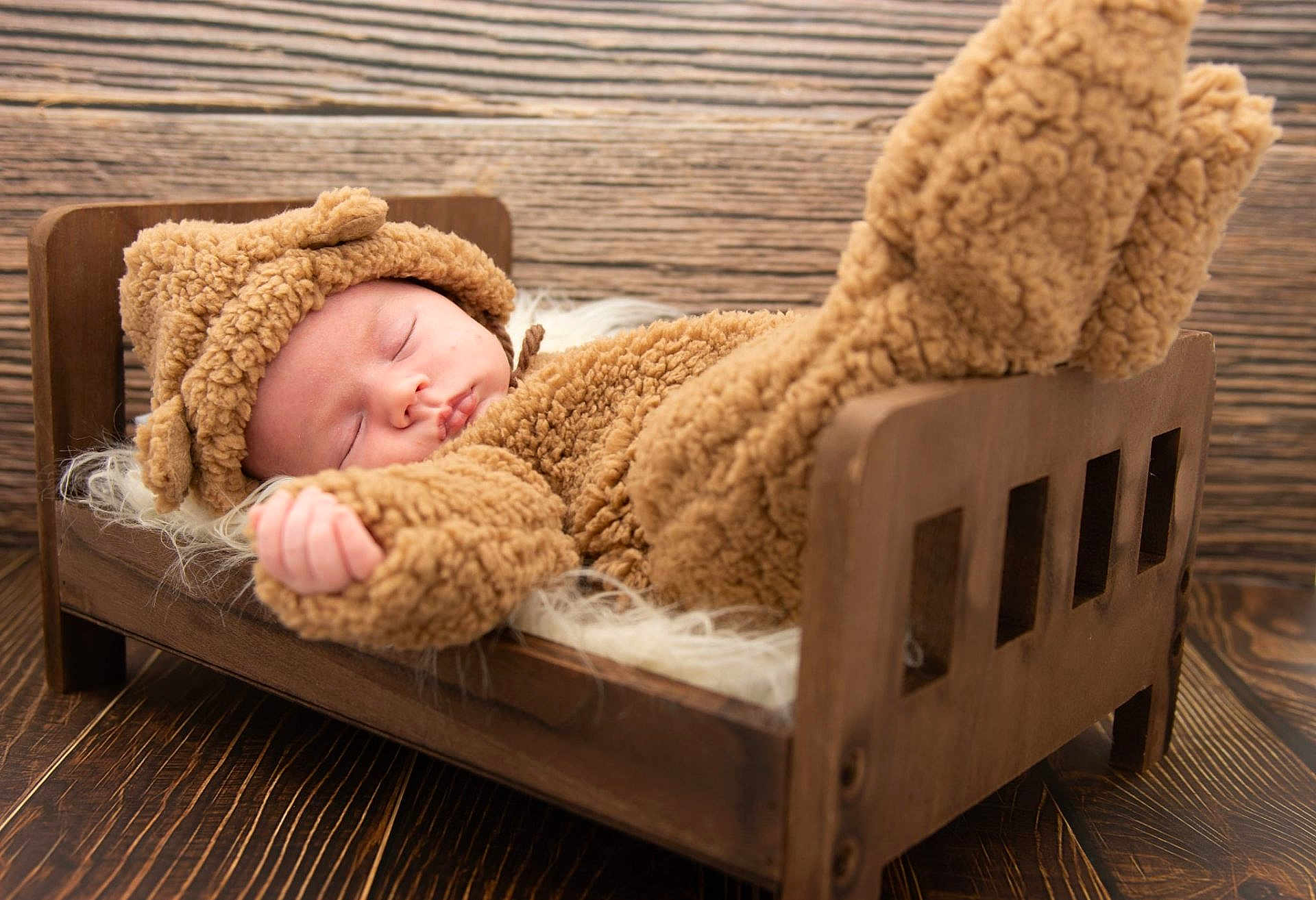 Henry is registered to the contest to win money with this photo: baby, sleeping, costume, bear, wooden_bed, fur_blanket, cozy, cute, infant, child, indoors, portrait, soft_texture, brown, warm, resting, peaceful, hat, hand, footwear