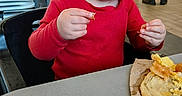 Tommus is registered to the contest to win money with this photo: child, toddler, baby, red_shirt, eating, food, pastry, breakfast, restaurant, dining, chair, table, indoor, portrait, close_up, smiling, messy_face, hands, family_dining, casual