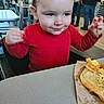 Tommus is registered to the contest to win money with this photo: child, toddler, baby, portrait, restaurant, dining, food, sandwich, bread, cheese, red_shirt, smiling, eating, messy_face, raised_hands, table, chairs, indoor, background_people, fast_food
