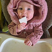 Izzahbella is registered to the contest to win money with this photo: baby, child, infant, portrait, pink_hood, hooded_jacket, winter_clothing, high_chair, snack, eating, hand, smiling, eyes, face, indoor, candid, close_up, feeding, baby_clothing, cozy