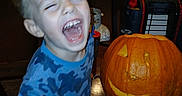 Ferris is registered to the contest to win money with this photo: child, toddler, boy, laughing, smiling, face, portrait, pumpkin, jack_o_lantern, halloween, pumpkin_carving, carving_tool, kitchen, indoors, home, table, blue_shirt, wooden_cabinets, holiday, autumn