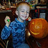 child, boy, smiling, portrait, pumpkin, jack_o_lantern, halloween, carving, kitchen, indoors, table, camouflage_shirt, blue_clothing, hand_tool, crafting, food, chair, home, celebration, photography