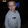 child, smiling, portrait, indoors, home, hoodie, puma, gray_clothing, blond_hair, blue_eyes, standing, happy, face, person, television, chandelier, living_room, flash_photography, casual_clothing, family_photo